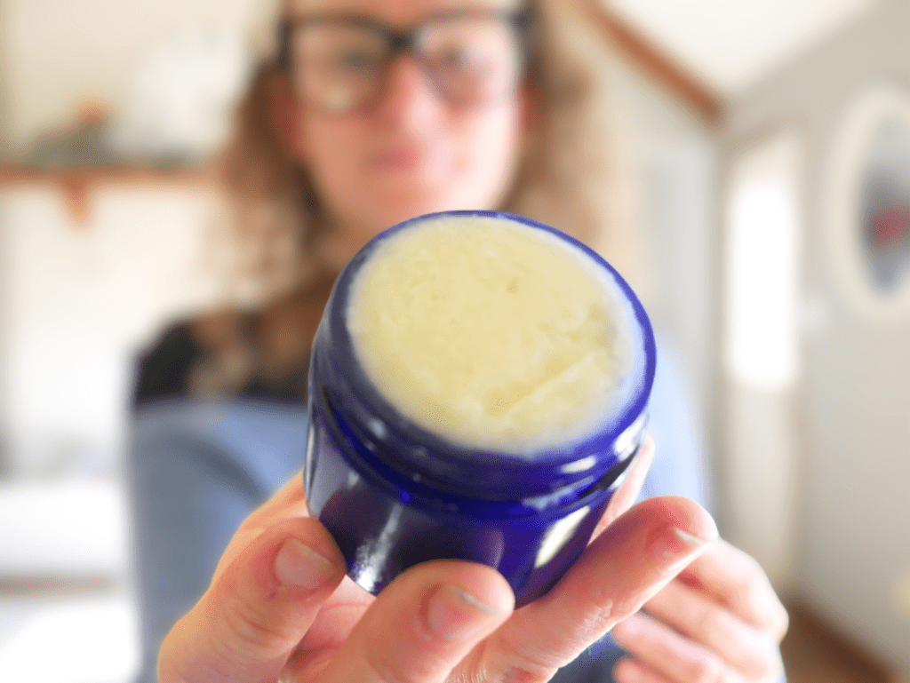 homemade vapor rub in a blue glass jar held by woman