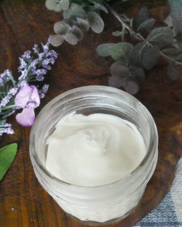 homemade anti-aging face cream with purple flowers and green leaves around jar