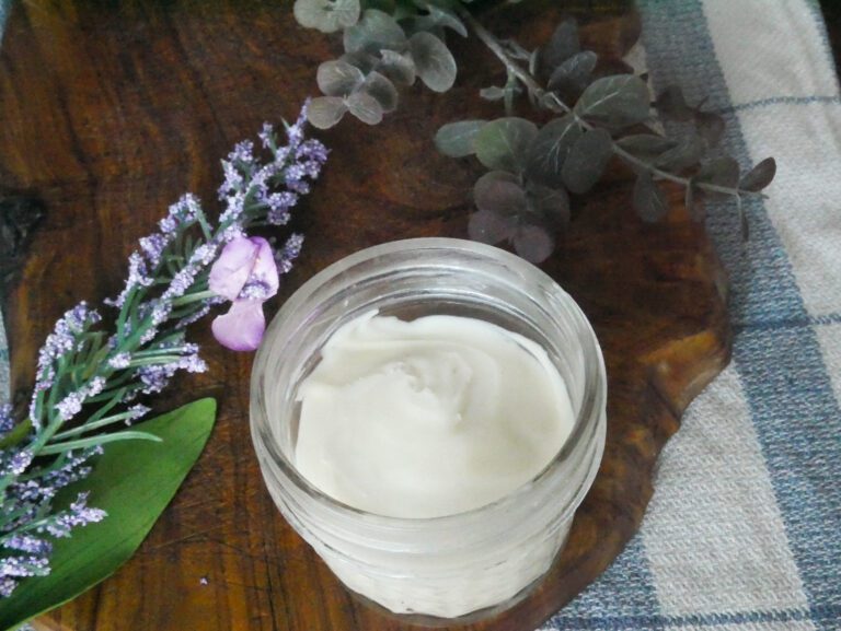 homemade anti-aging face cream with purple flowers and green leaves around jar