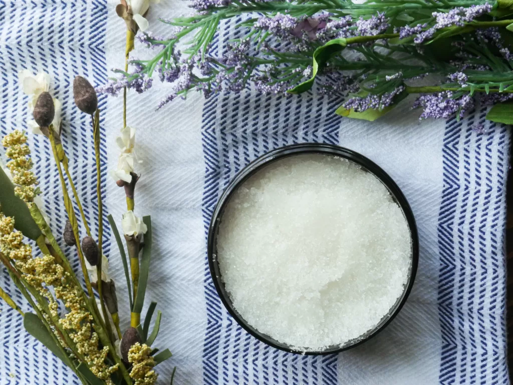 homemade sugar scrub in container with chamomile and lavender laying around it.