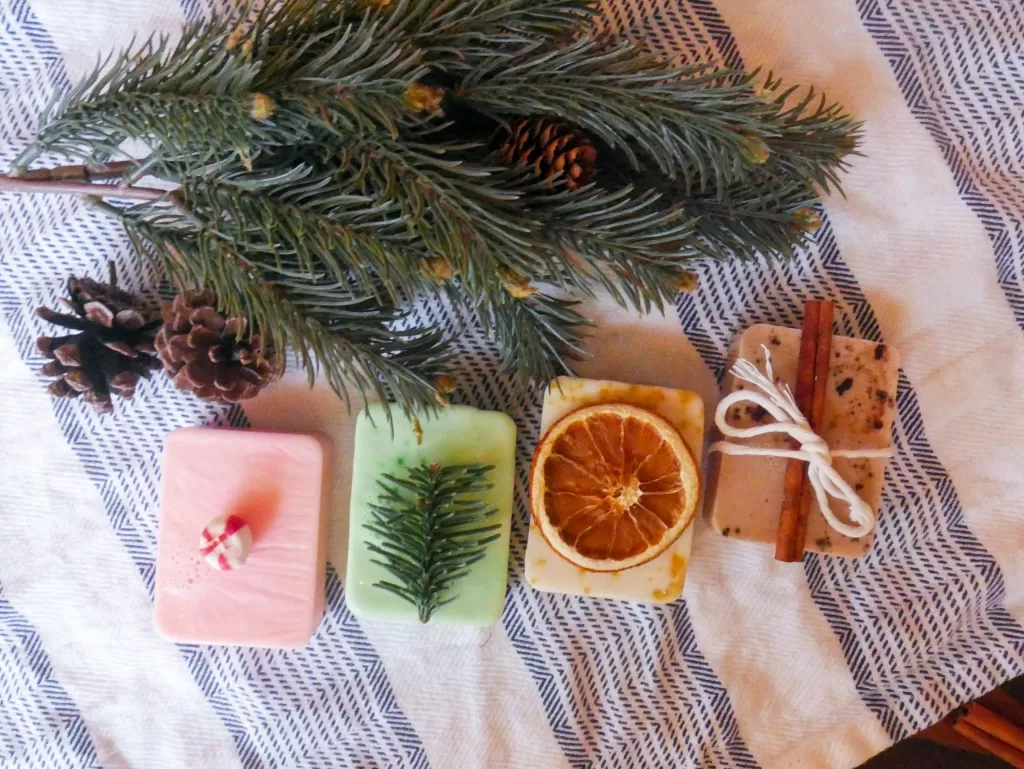 4 homemade melt and pour christmas soaps next to an evergreen branch