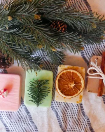 4 homemade melt and pour christmas soaps next to an evergreen branch