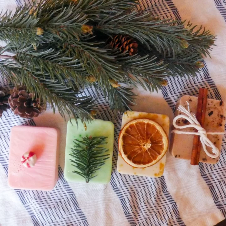 4 homemade melt and pour christmas soaps next to an evergreen branch
