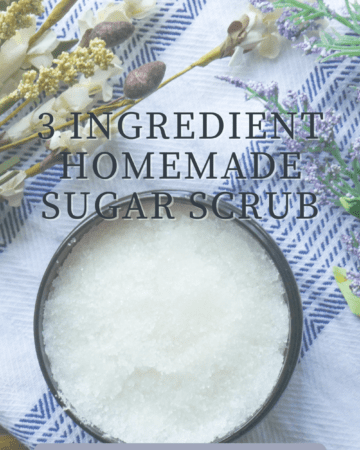 3 ingredient homemade sugar scrub words with sugar scrub in brown container surrounded by chamomile and lavender in background