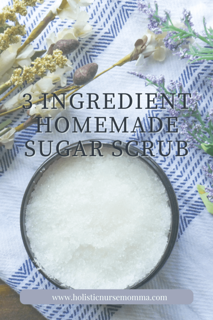 3 ingredient homemade sugar scrub words with sugar scrub in brown container surrounded by chamomile and lavender in background