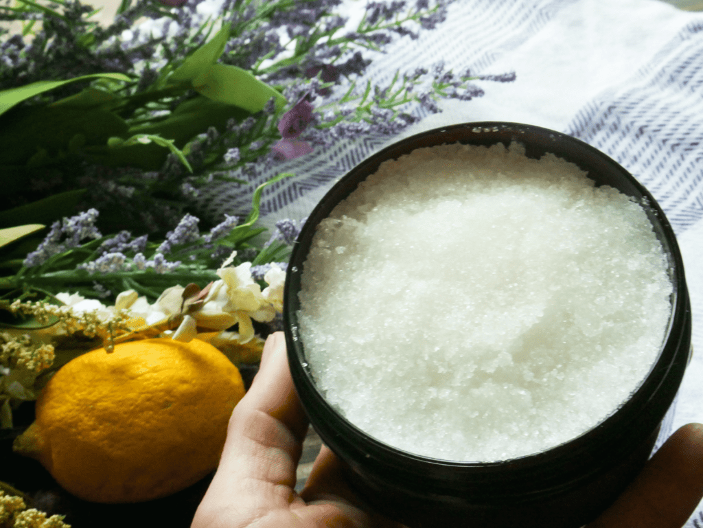 homemade sugar scrub being help in front of flowers and a lemon