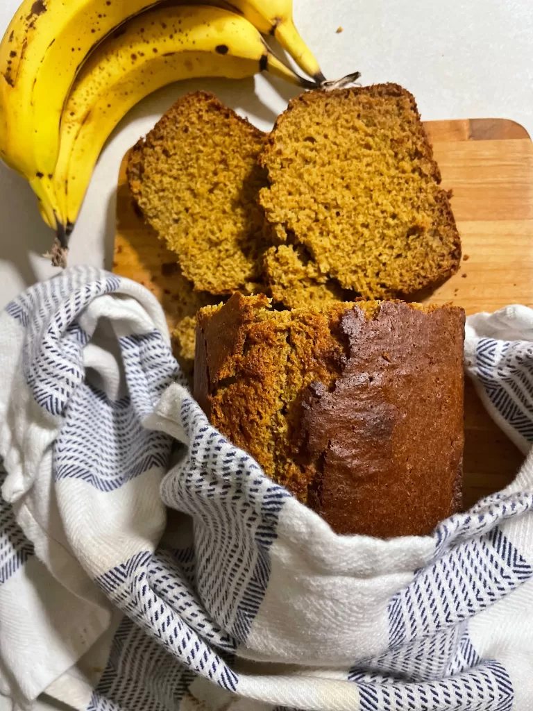 banana bread on a cutting board with a blue and white striped towel wrapped around it