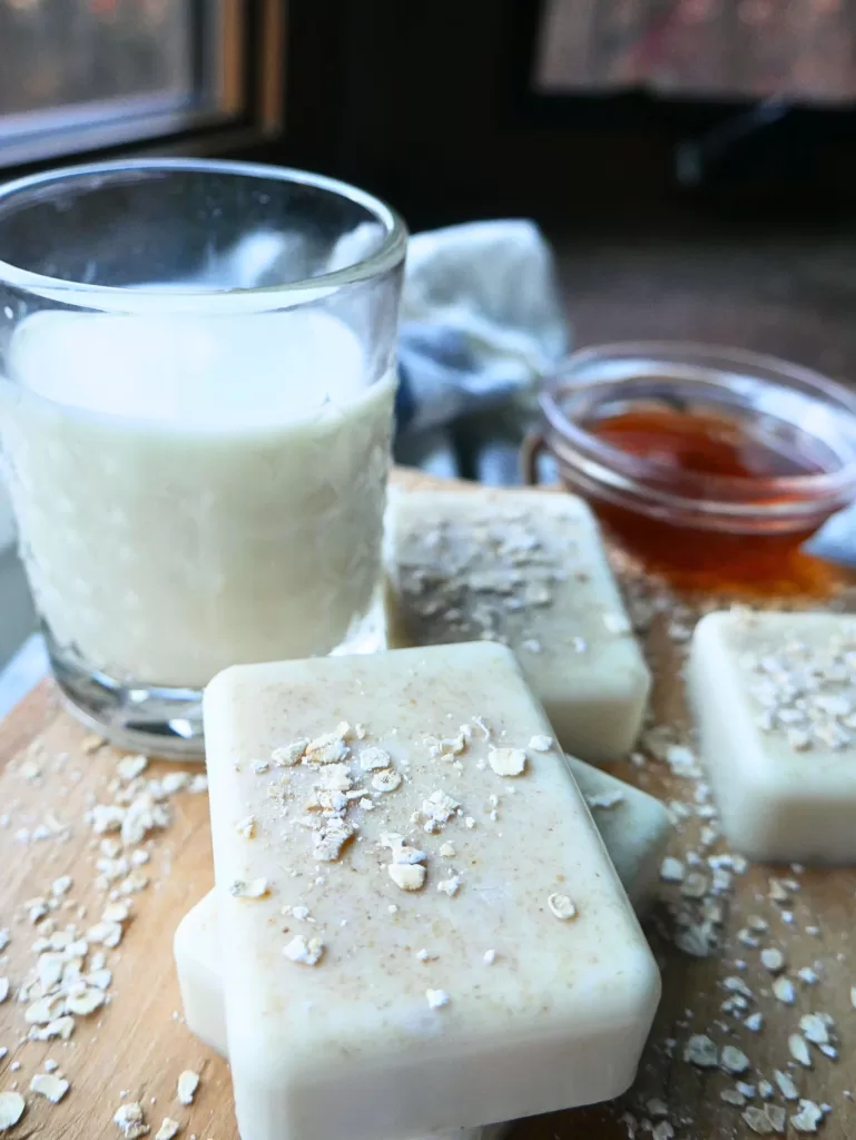 homemade soap on a wooden cutting board with glass cup of milk and glass jar of honey