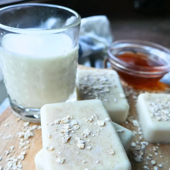 homemade soap on a wooden cutting board with glass cup of milk and glass jar of honey