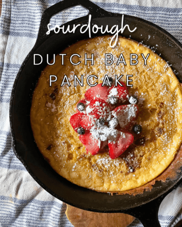 sourdough dutch baby pancake with fruit and powdered sugar on top in a cast iron skillet