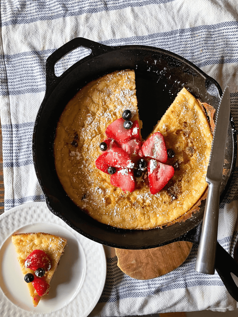 sourdough discard dutch baby pancake in cast iron skillet with one slice cut out