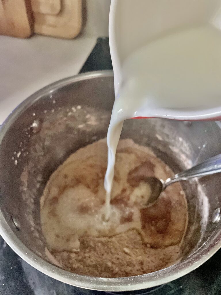 pouring milk into stainless steel pot with homemade chocolate pudding ingredients inside