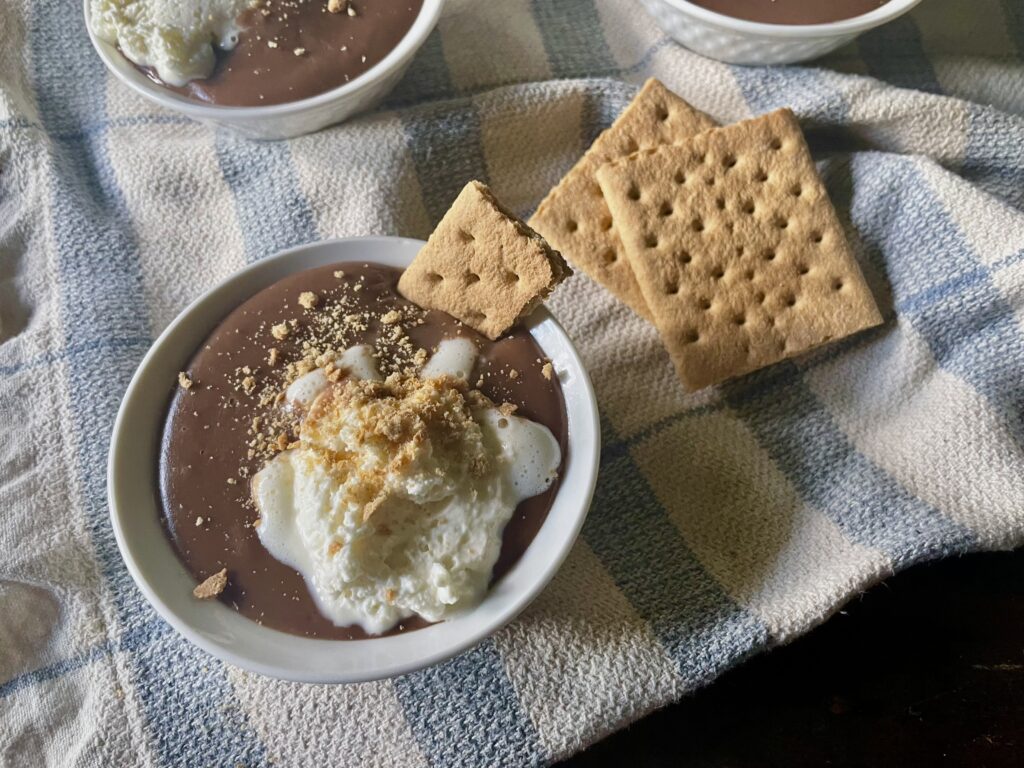 homemade chocolate pudding in small white bowl with graham crackers on top