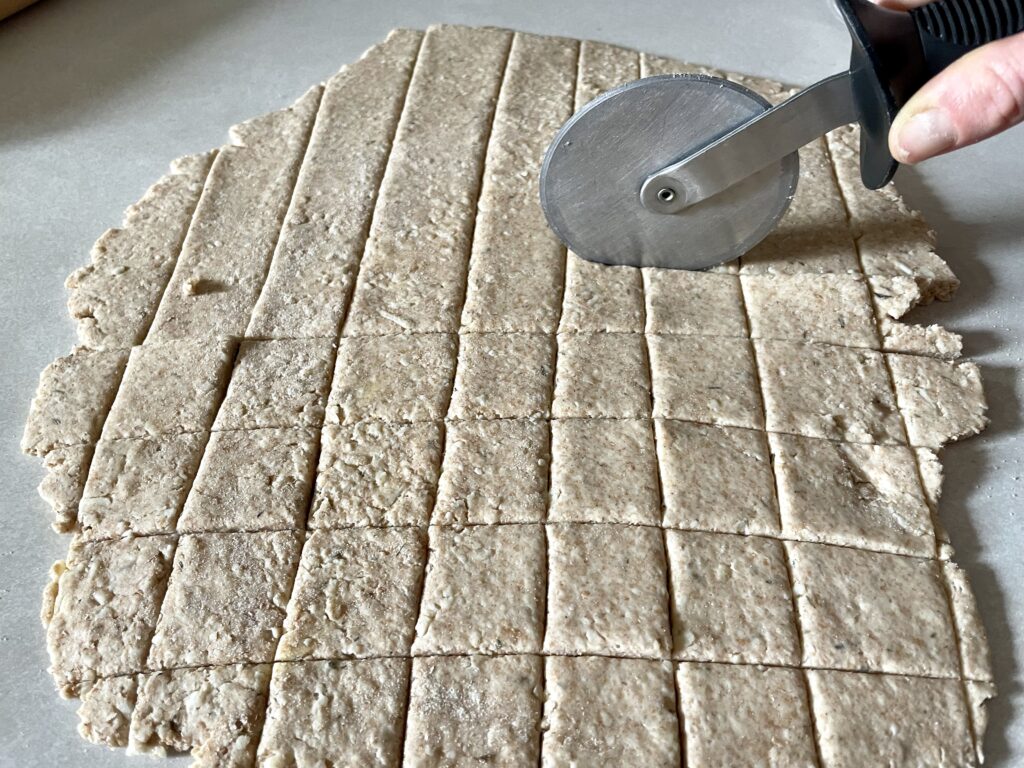 pizza cutter cutting the dough of sourdough discard crackers made with freshly milled flour and cheese