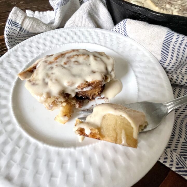 1 gluten free cinnamon roll sitting on a white plate with one bite cut out