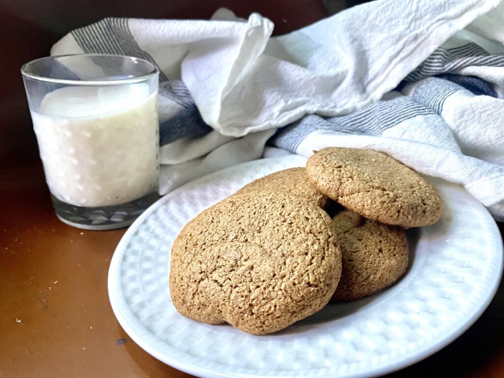 fresh milled flour gingersnap cookies on a white plate with a glass of milk next to it