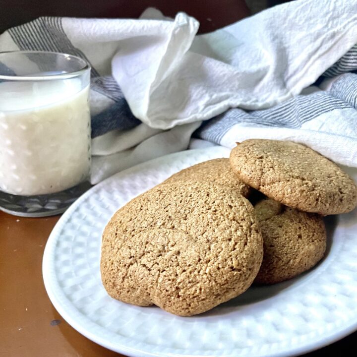 fresh milled flour gingersnap cookies on a white plate with a glass of milk next to it