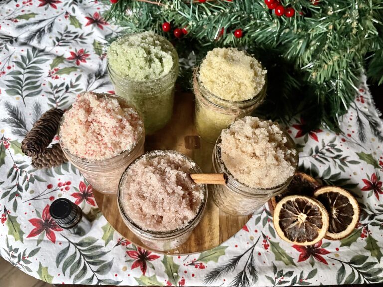 5 different Christmas sugar scrubs on a Christmas themed cloth