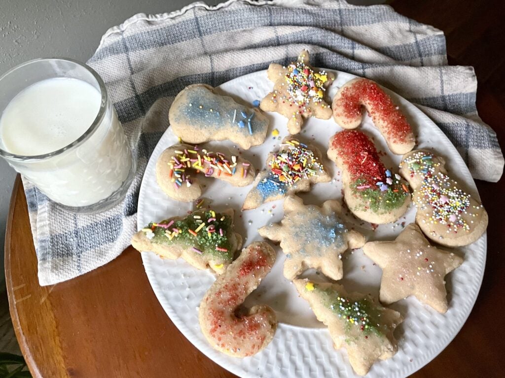 iced and sprinkled fresh milled flour sugar cookies on white plate with glass of milk