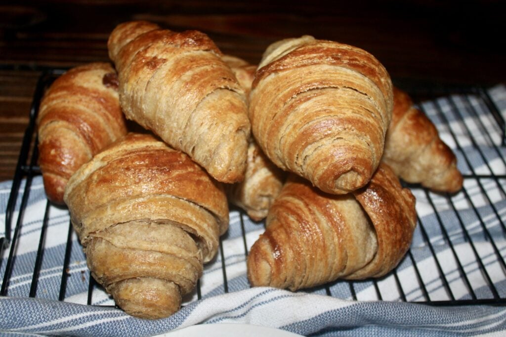fresh milled flour sourdough croissants stacked in a pile on a wire cooling rack