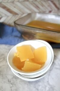 cubed homemade orange jello in a small white bowl with a pan of healthy homemade orange jello in the background