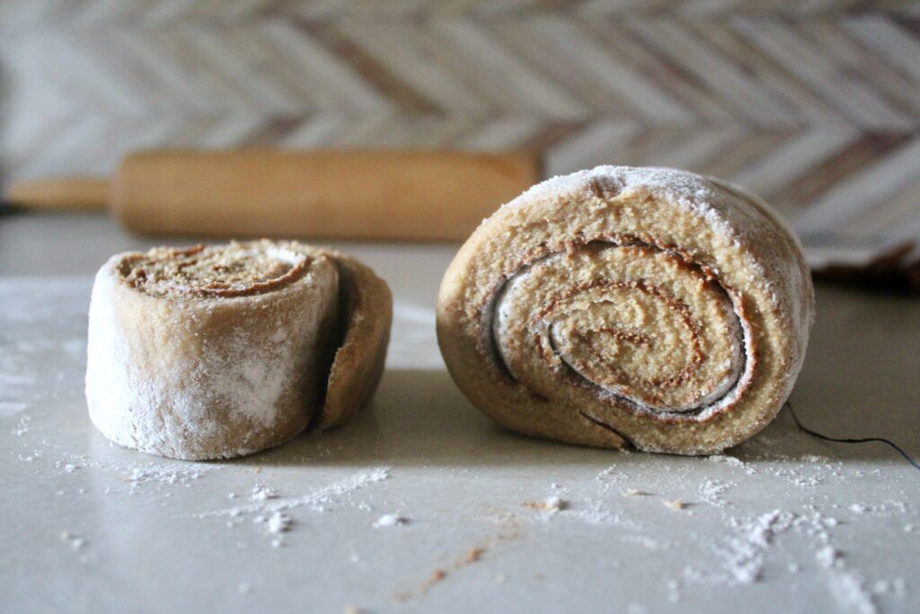 cutting rolled, unbaked fresh milled flour sourdough cinnamon rolls with rolling pin in background