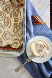 one no refined sugar fresh milled flour sourdough cinnamon roll with cream cheese icing on white plate next to pan of cinnamon rolls