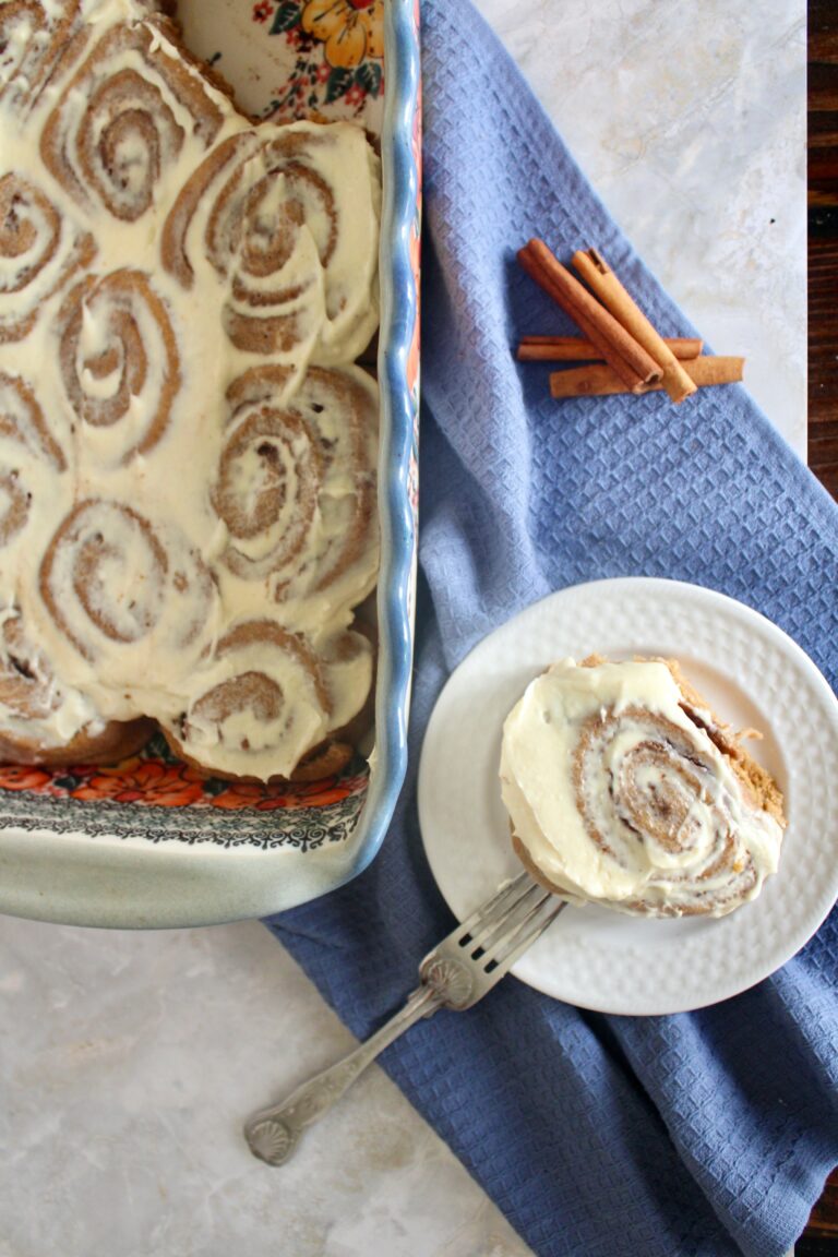 one no refined sugar fresh milled flour sourdough cinnamon roll with cream cheese icing on white plate next to pan of cinnamon rolls