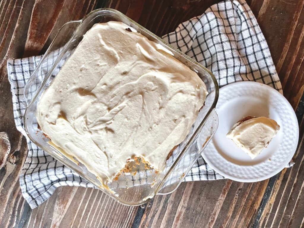 fresh milled flour buttermilk carrot cake with cream cheese frosting in a glass pan with a slice on a plate next to it